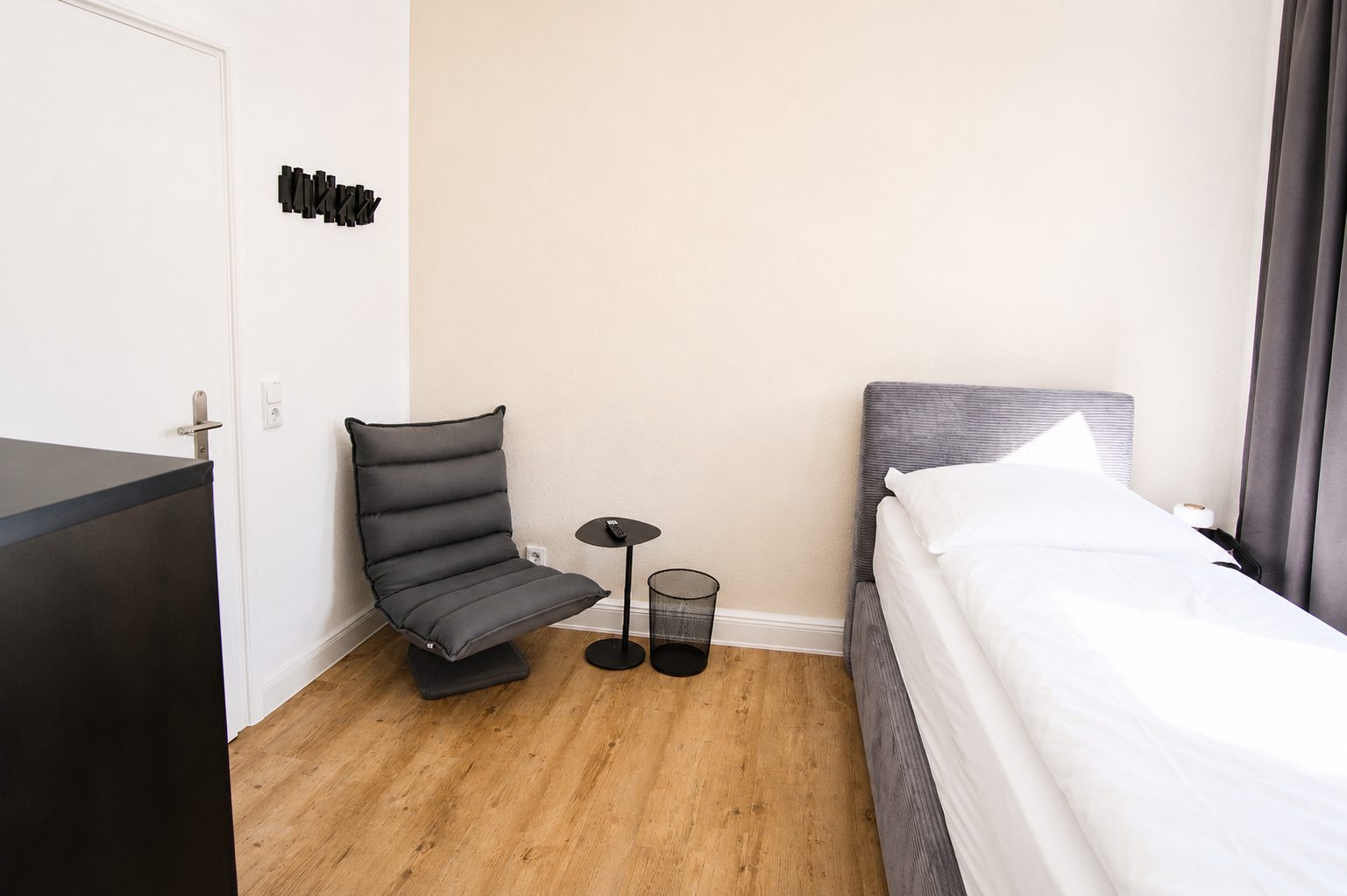 Zimmer 6 mit Bett, Loungesessel, Beistelltisch und Wandgarderobe